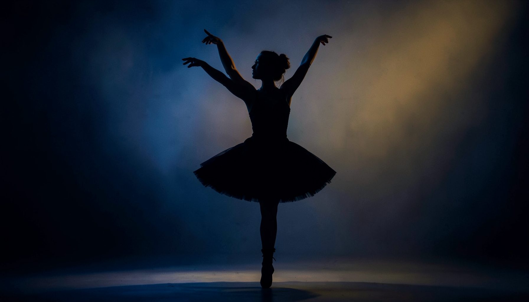 Silueta de una bailarina en un estudio con luz cálida y tenue, tonos azul profundo y dorado