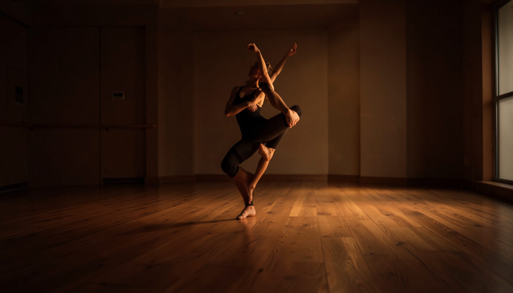 Superficie de piso de madera de un estudio de danza, iluminada por una luz cálida y tenue que crea un ambiente sereno y profesional, en tonos marrones profundos y dorados suaves.